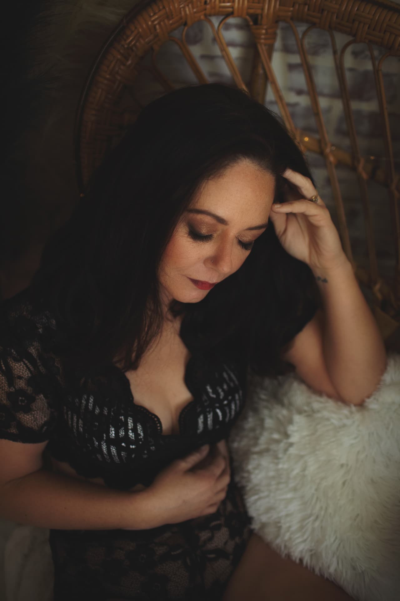 Woman in black lace seated in a wicker chair, looking down