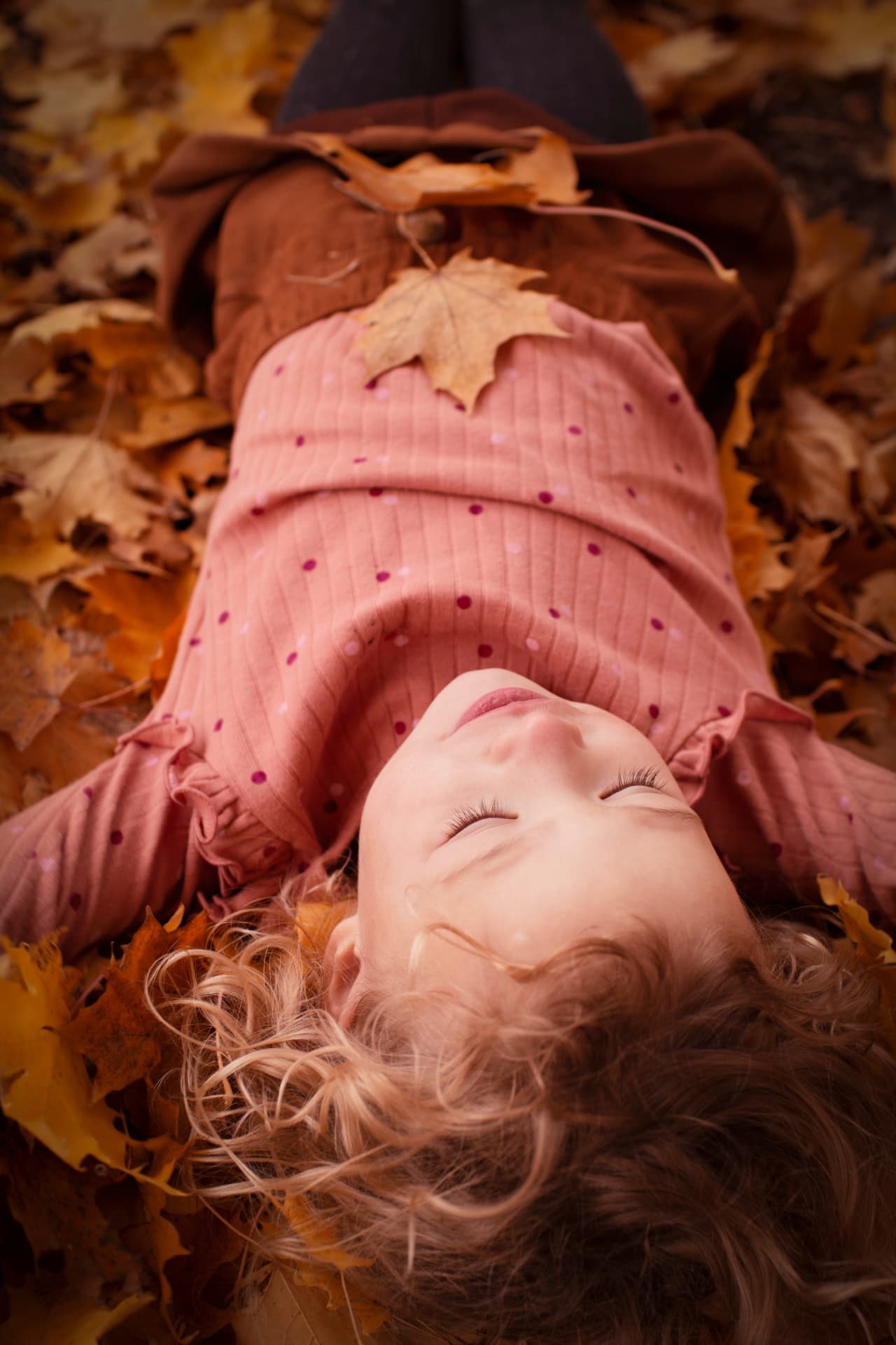Child lying back among autumn leaves