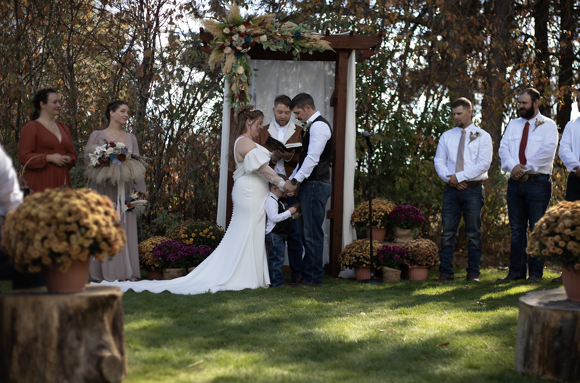Bride and groom exchanging vows with their son at an outdoor autumn ceremony